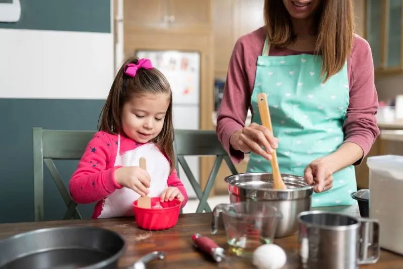 Mignonne petite fille portant un tablier et s'apprêtant à faire des biscuits avec sa mère dans la cuisine.