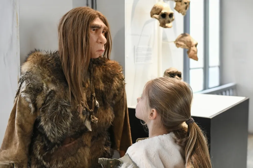 Une jeune fille regarde la statue d'un homme des cavernes dans un musée