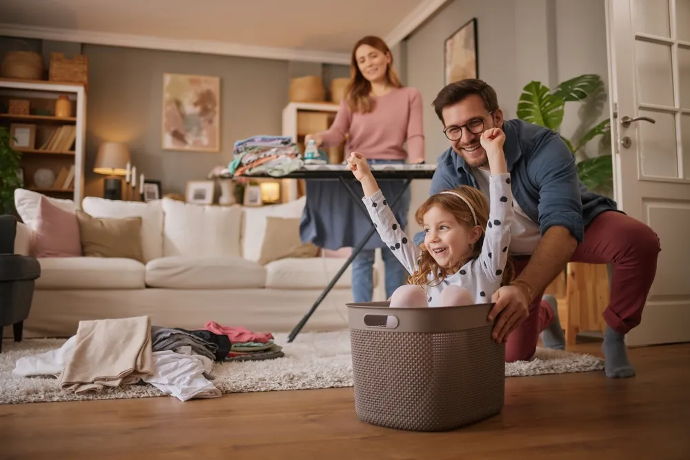 Fille et papa riant en jouant avec le panier à linge dans le salon
