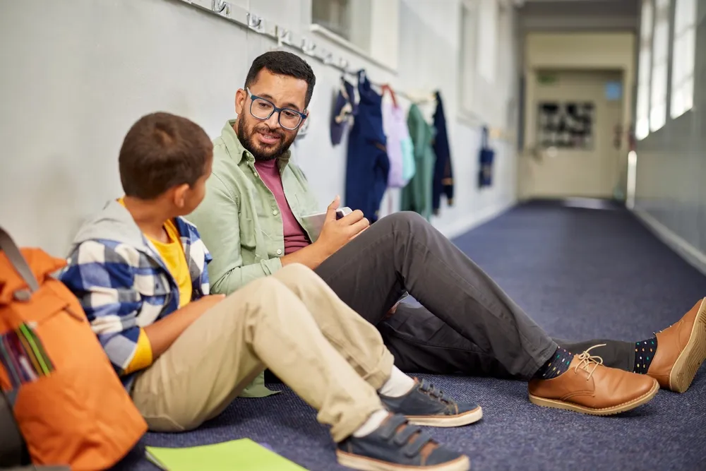 Un jeune psychologue parle à un garçon déprimé à l'école, assis par terre dans le couloir de l'école