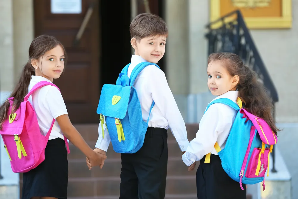 Deux filles et un garçon se tenant la main avant d'entrer à l'école