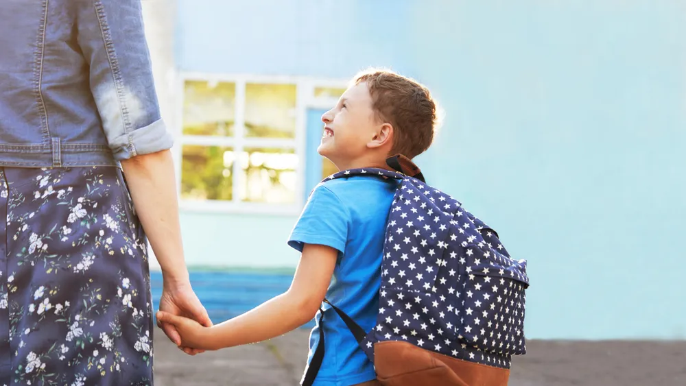 Un enfant tenant la main de sa mère et souriant avant d'entrer à l'école